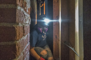 A Nechama volunteer wears a headlamp shining into a dark space near a chimney.