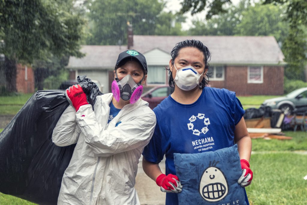 Michigan program extended. two volunteers pause for a photo in the rain, carrying items out of a flood damaged home in Detroit, Michigan.
