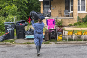 Michigan Program Extended- AmericorpsNCCC member carries bag of flooded debris to a pile on a curb outside the home